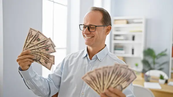 Smiling middle age man confidently handling dollars in his office, a happy worker showcasing success in business