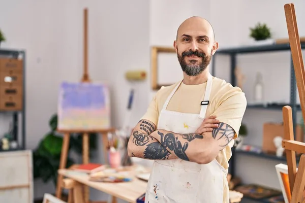 Young bald man smiling confident standing with arms crossed gesture at art studio
