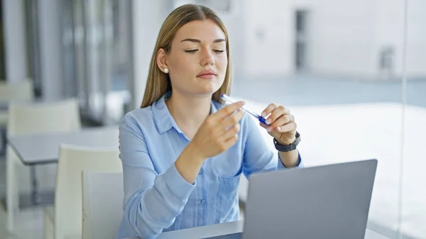 Young blonde woman business worker using laptop looking pen at office