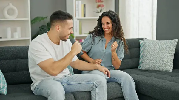 Man and woman couple singing song using remote control as a microphone at home