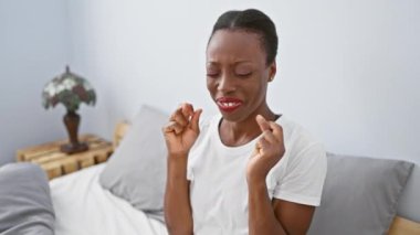 Neşeli Afro-Amerikalı kadın rahat bir yatakta uzanıyor, el işareti yapıyor, gözleri umut ve pozitiflikle kapalı, rahat bir yatak odasında. Şansın sembolü ve dileklerin ifadesi..