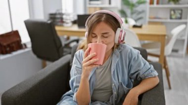 Genç sarışın iş kadını müzik dinliyor ofiste kahve içiyor.