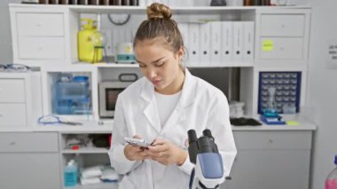Genç ve güzel İspanyol bilim adamı laboratuvarda gülümseyen akıllı telefon kullanıyor.
