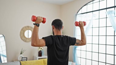 Genç İspanyol adam dambılları evde tersten eğitiyor.