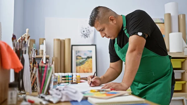年轻英俊的拉丁画家专心致志地在室内的艺术工作室上绘画课 站在办公桌前 用画布和画笔表现他的热情爱好 — 图库照片