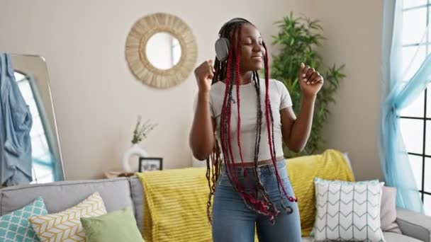 快乐的非洲裔美国女人摇着辫子 听着音乐 满怀信心地在客厅里跳舞 一边在家里享受着悠闲的生活 一边笑着 — 图库视频影像