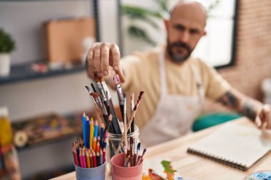 Sanat stüdyosunda fırça tutan kel genç bir sanatçı.
