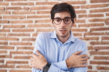 Tuğla duvar arkasında duran İspanyol genç adam yüzünde üzgün ve şok ifadesiyle kış soğuğu için titriyor ve donuyor. 