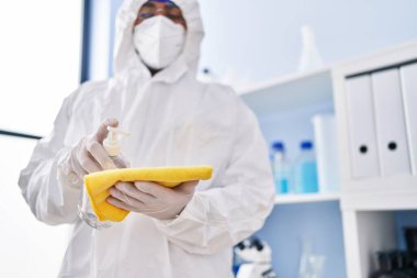 Tıbbi maske takan genç İspanyol bilim adamı laboratuarda kumaşa dezenfektan jeli döküyor.