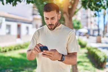 Genç İspanyol bir adam parkta akıllı telefon kullanıyor.