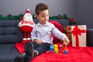 Sevimli İspanyol bebek, evdeki Noel süslemesinde koltukta oturmuş oyuncak trenle oynuyor.