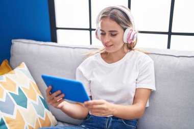Sarışın genç kadın dokunmatik yastıkta video izliyor. Evdeki kanepede oturuyor.