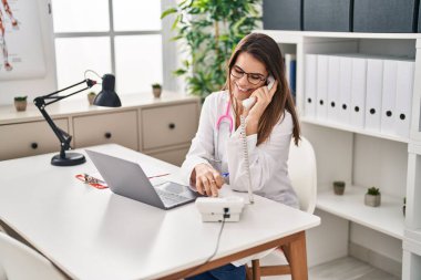 Genç, güzel, İspanyol bir kadın. Laptop kullanıyor. Klinikte telefonla konuşuyor.
