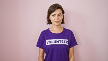 Sersemletici genç İspanyol kadın, bıkmadan bağışlar üzerinde çalışan, fedakarlık ve birlik saçan, izole edilmiş pembe bir arka planda duran, ciddi bir ifadeyi resmeden bir gönüllü.