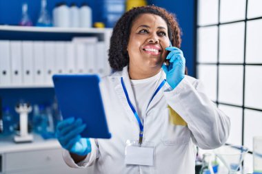 African american woman scientist talking on smartphone using touchpad at laboratory