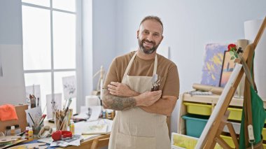 Kendine güvenen genç sanatçı, yaratıcılıkla dolup taşan, sanat stüdyosunda çapraz kollarla dikilen, tuvalin tadını çıkaran, sınıfın, çizimin ve resmin ustası, fırçaların tuttuğu,.
