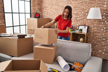 Young beautiful hispanic woman smiling confident holding package at new home