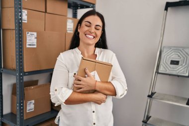 Genç, güzel, İspanyol bir kadın. İşçi bürosunda bir paket tutuyor.