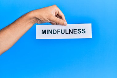 Hand of caucasian man holding paper with mindfulness word over isolated blue background