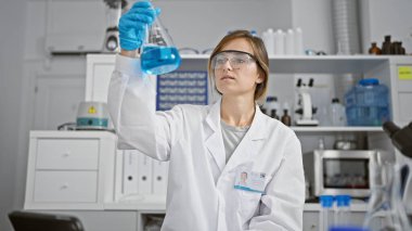 Güzel sarışın bilim adamı iş başında, güvenlik eldiveni takan genç bir kadın yüksek teknoloji laboratuarında test tüpünü inceliyor.