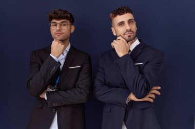 İş kıyafetleri giymiş iki İspanyol iş adamı kameraya kollarını kavuşturup gülümseyen ve çenesini kaldırmış bir şekilde bakıyorlar. Olumlu düşünmek. 