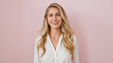 Parlak ve neşeli, kendine güvenen, pozitif enerji saçan, neşeli bir şekilde gülümseyen ve pembe arka planda tek başına duran genç, sarışın bir kadın.!