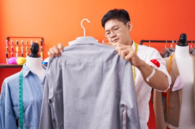 Young chinese man tailor holding shirt at atelier