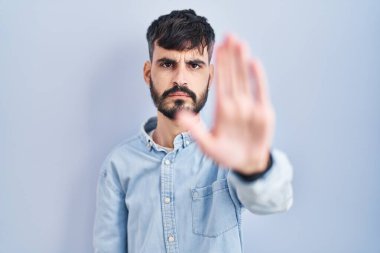 Mavi arka planda duran sakallı genç İspanyol bir adam avucunun içi gibi şarkı söylemeyi kesiyor. Yüzünde olumsuz ve ciddi bir jest olan uyarı ifadesi. 