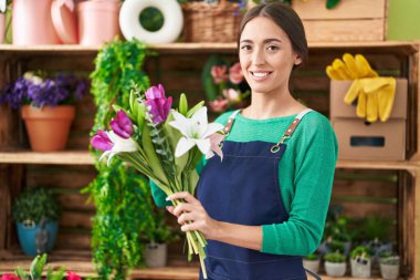 Young beautiful hispanic woman florist holding bouquet of flowers at flower shop