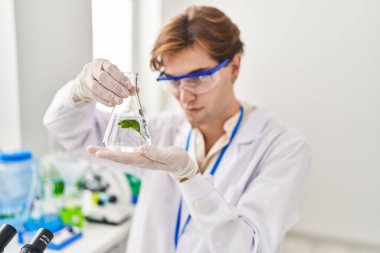 Young caucasian man scientist holding test tube with plant at laboratory
