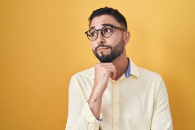 İspanyol genç adam iş kıyafetleri giyiyor ve elleri çenesinde gözlük takıyor soru sormayı düşünüyor, düşünceli yüz ifadesi. Düşünceli bir yüzle gülümsüyor. şüphe kavramı. 