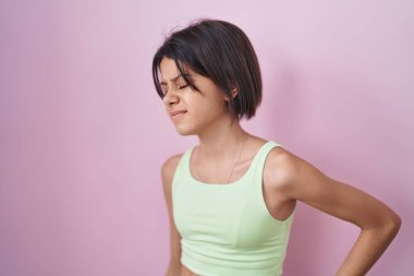 Pembe arka planda duran genç bir kız sırt ağrısı çekiyor, elleriyle dokunuyor, kas ağrısı çekiyor. 