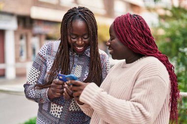 Sokakta akıllı telefon ve kredi kartı kullanan Afrikalı Amerikalı kadın arkadaşlar