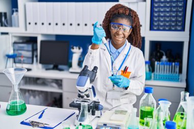 Laboratuvarda test tüpüne sıvı döken Afrikalı Amerikalı kadın bilim adamı.