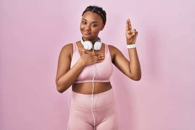 Spor kıyafetleri ve kulaklıkları takan, elleri göğsünde ve parmakları havada küfreden, sadakat yemini eden Afro-Amerikan bir kadın. 