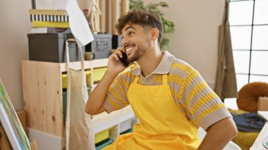 Kendine güveni tam bir Arap, gülümseyen bir sanat öğrencisi, canlı üniversite atölyesinde resim ve tuvallerinin arasında akıllı telefonuyla heyecanla konuşuyor..