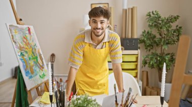 Gülümseyen, kendine güvenen genç Arap sanatçı, mutlu hobisinin keyfini çıkarıyor, resim yapıyor ve bir kahkaha atölyesinde neşe çiziyor.