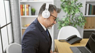 Yakışıklı, gri saçlı, İspanyol bir iş adamı, rahat bir andan zevk alıyor iş yerinde müzik dinliyor, kulaklıklarını takıyor.