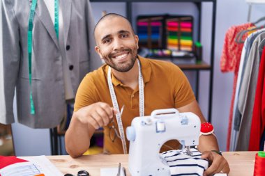 Young latin man tailor smiling confident using sewing machine at atelier