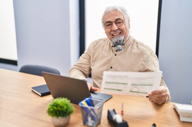 Ofiste dizüstü bilgisayar okuyarak orta yaşlı, kır saçlı bir iş adamı.