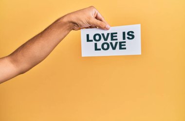 Hand of caucasian man holding paper with love is love message over isolated yellow background