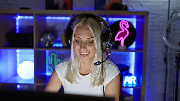 Laughing blonde woman streamer, playing video game, confident in gaming room, streaming night entertainment
