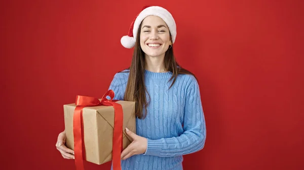 年轻的高加索女人头戴圣诞礼帽 头戴孤立的红色背景 带着礼物 — 图库照片