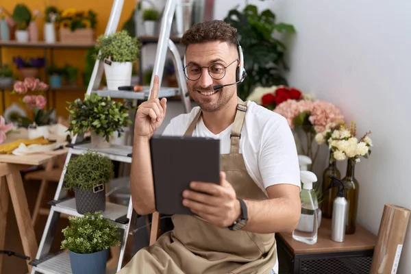 Hispanic man with beard working at florist shop doing video call smiling with an idea or question pointing finger with happy face, number one