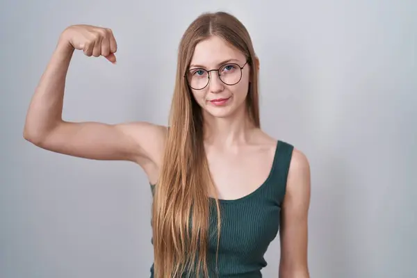年轻的高加索女人站在白种人的背景上 强壮有力地展示臂膀肌肉 自信而自豪 — 图库照片