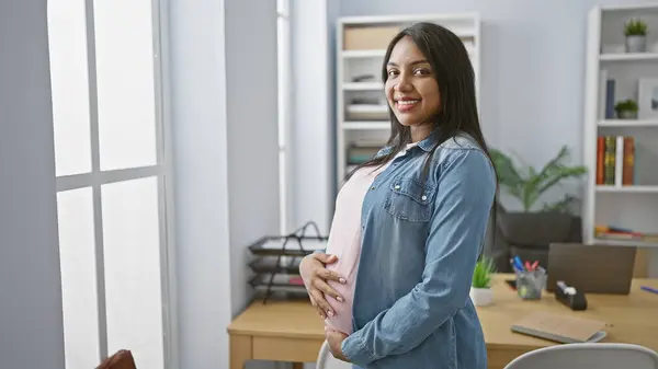 年轻孕妇在办公室工作时 满脸笑容自信地摸着肚子 体现了母性和商业上的成功 — 图库照片