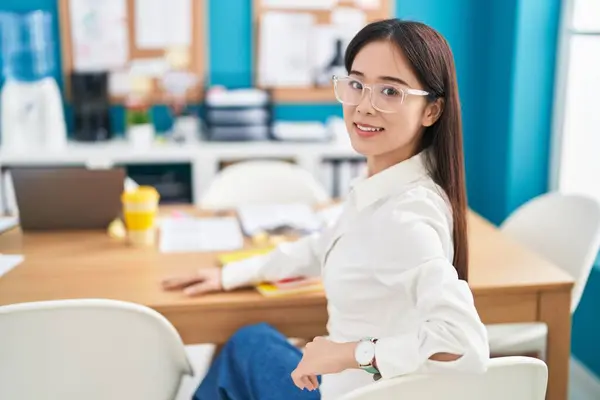 Young chinese woman business worker smiling confident sitting on table at office