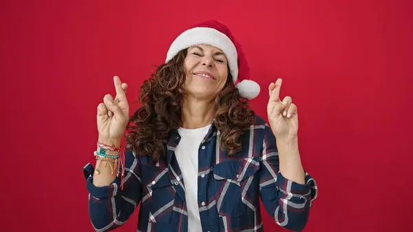 Латиноамериканка Средних Лет Носит Рождественскую Шляпу Скрестив Пальцы Удачу Изолированном — стоковое фото