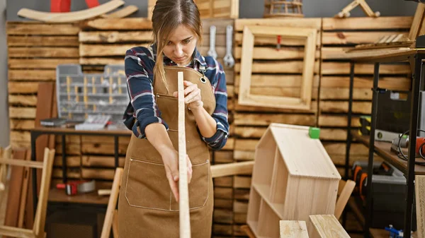 Beautiful young blonde woman, a professional carpenter, proudly holding a wood plank at her carpentry workshop, embodying the strength of industrious females in the construction industry
