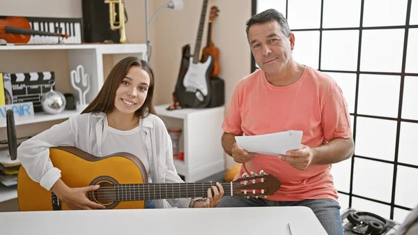 Smiling male and female musicians engrossed in a classic guitar lesson at a cozy music studio, sharing their love for music.